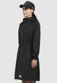 Černá voděodolná bunda se staženým pasem, přiléhavou kapucí a zipovými kapsami. Vlastnosti zahrnují elastické manžety a minimalistický design. Černá kšiltovka s logem.