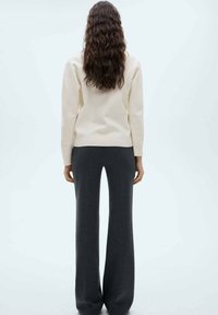 Krämfärgad tröja med långa ärmar och rak passform, matchad med högmidjade byxor i vid modell i kolgrått. Släta texturer, minimalistisk design.