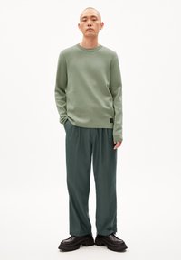 Suéter de cuello redondo verde claro y pantalones anchos verdes oscuros combinados con zapatos negros gruesos, sobre un modelo frente a un fondo blanco.