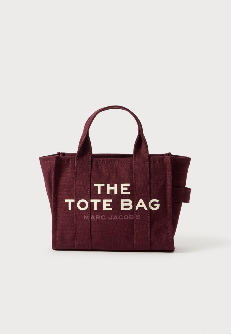 Sac fourre-tout en toile bordeaux avec deux poignées courtes, comportant un grand texte blanc "LE SAC FOURRE-TOUT" et en dessous, un plus petit "MARC JACOBS".