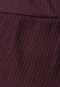 Gros plan d’un tissu tricot côtelé violet foncé avec des coutures visibles le long d’une couture horizontale.