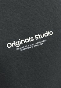 Tessuto nero con una superficie liscia e testo bianco che recita "Originals Studio" e "offerto da JACK & JONES."