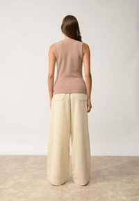 Beżowy bezrękawnik o dzianinowej strukturze w połączeniu z szerokimi, kremowymi spodniami z prążkowanej tkaniny, posiadającymi tylne kieszenie i luźny krój.