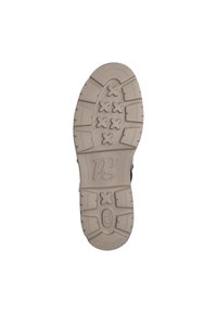 Suela de zapatilla negra con una suela de goma beige texturizada, que presenta un patrón geométrico y un detalle de logo moldeado.