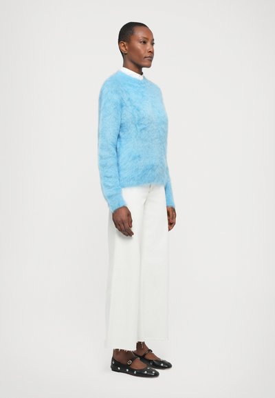 Pull bleu clair, moelleux, à manches longues ; porté sur un pantalon large blanc et des chaussures noires avec des accents argentés.
