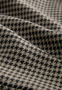 Tissu à motif pied-de-poule noir et beige avec une texture visible et des plis souples créant une surface ondulée.