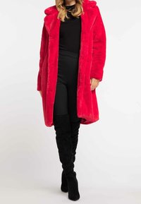 Cappotto in pelliccia sintetica di un rosso brillante con cappuccio, maniche lunghe e un design morbido di lunghezza media. Abbinate a leggings neri e stivali neri alti fino alla coscia.