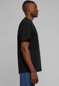 Black cotton T-shirt with short sleeves, classic fit, and crew neckline. Smooth texture; paired with blue denim jeans. Side view.