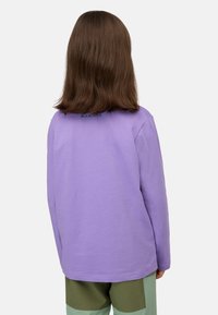 Lila Langarm-T-Shirt aus Baumwolle mit Rundhalsausschnitt und Logodetail auf dem Rücken. Kombiniert mit grünen Shorts.