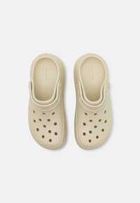 Sabots beige clair en matériau ressemblant au caoutchouc. Dotés de multiples trous de ventilation, d'une bride arrière pour un maintien sécurisé et d'une semelle intérieure texturée.