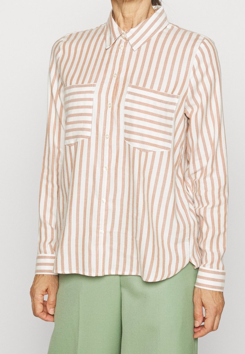 Camicia a righe con bottoni in morbido bianco e pesche, dotata di due tasche sul petto e un orlo leggermente curvo. Realizzata in tessuto leggero.