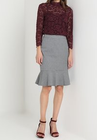 Burgundy spets långärmad topp över en grå blyertskjol med utställd nederkant, matchad med burgundy klackar med remmar. Mjuk textur och subtila mönster.