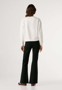 Biela mikina s okrúhlym výstrihom, rebrovanými manžetami a voľným strihom, skombinovaná s rozšírenými tmavými džínsami a vínovými topánkami.