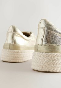 Baskets métalliques dorées avec une finition texturée, présentant une semelle en corde blanche épaisse et un design bas au niveau du talon.