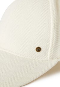 Biała czapka z fakturą jodełki. Ma zaokrąglony daszek i mały, okrągły, mosiężny emblemat z przodu.