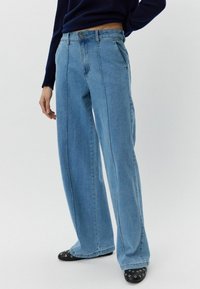 Svijetloplave široke traperice s visokim strukom, zatvaranjem na dugme, prednjim i stražnjim džepovima te ravnim šavovima. Glatka denimska tekstura.