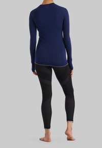 Námořnický modrý top s dlouhým rukávem a texturovaným tělem spolu s přiléhavými černými legínami se vzorovanými panely a žebrovanou texturou. Oba kousky jsou přiléhavé.