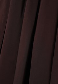 Braun gefalteter Stoff, der eine glatte Textur mit leichtem Glanz zeigt, aus leichtem Material gefertigt, mit tiefen, reichen Farbvariationen.