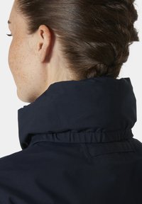 Granatowa kurtka przeciwdeszczowa z wysokim kołnierzem, charakteryzująca się gładką fakturą i marszczeniami przy szyi. Materiał jest lekki i wodoodporny.