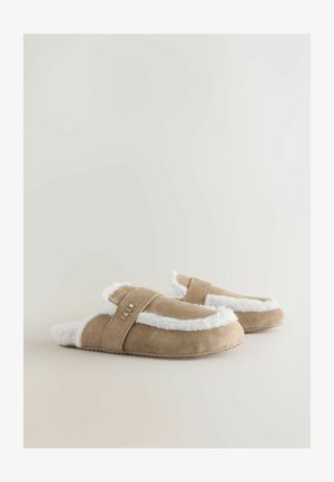 Dzelteni zamša čības ar baltu kažokādas apdari un iekšpusi. Aprīkotas ar siksnu ar zeltītu uzrakstu. Mīksta tekstūra un plakana zole.