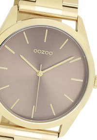 Montre-bracelet dorée avec un cadran marron mat, des index horaires minimalistes et un bracelet en métal lisse. Comprend un boîtier rond classique.