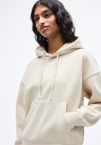 Μπεζ φούτερ με απαλό ύφασμα, που διαθέτει τσέπη καγκουρό, κορδόνια και ριμπ μανσέτες. Καθημερινή, φαρδιά εφαρμογή με κουκούλα.