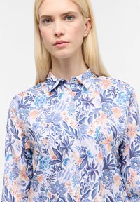 Bloemenoverhemd met knopen, met blauwe, perzikkleurige en witte patronen. Het materiaal heeft een gladde textuur en een klassieke kraag met knopen.