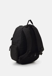 Musta reppu, jossa on pehmustetut hihnat, teksturoidut sivut ja pieni etutasku. Ominaisuuksia ovat säädettävä varustus ja verkkomateriaali ilmanvaihtoa varten.