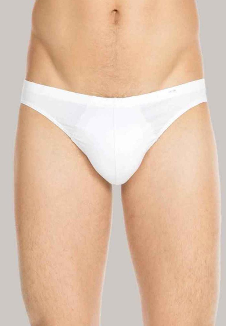Torse masculin portant un slip blanc uni, montré de la taille aux cuisses supérieures sur un fond gris neutre.
