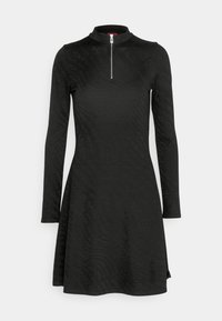 Robe noire à manches longues avec un col montant et une fermeture éclair à l'avant. Présente un motif texturé sur toute la surface et s'évase légèrement à l'ourlet.