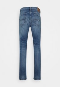 Medium wash denim jeans, rakad design, femficksstil, kraftigt tyg, synliga sömmar, läderlogotyp på midjebandet.