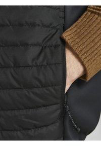 Czarna pikowana kurtka puchowa z brązowym, prążkowanym, dzianym mankietem, wyposażona w boczną kieszeń i teksturowane poziome przeszycia. Zapięcie na zamek błyskawiczny z detalem w postaci paska do ściągania.