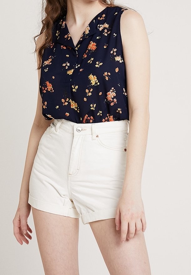 Námořnická květinová bezrukávová blůza s límečkem v kombinaci s bílými džínovými šortkami, které mají ohrnuté lemy a přední zapínání na knoflíky.