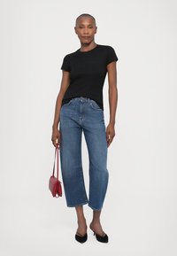 Black crew-neck t-shirt paired with high-waisted, straight-leg light blue jeans. Model holds a small red handbag; black heels complete the outfit.