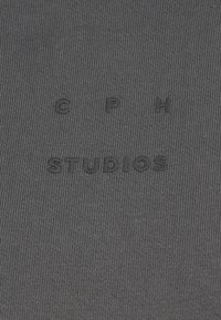 Un tissu gris côtelé présente le texte en relief "C P H STUDIOS" au centre, avec une texture lisse et un design minimaliste.