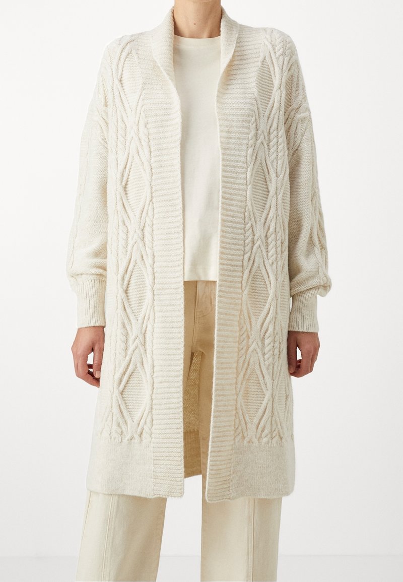 Dlouhý kardigan s otevřeným předním dílem v měkkém béžovém pleteném materiálu. Obsahuje texturované diamantové vzory a žebrované manžety. Nosi se přes světlý top a kalhoty.