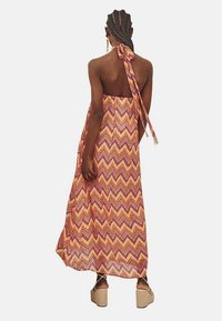 Vestido maxi con un patrón de zigzag en naranja, rosa y amarillo. Diseño sin espalda con un lazo al cuello y tela ligera y fluida.