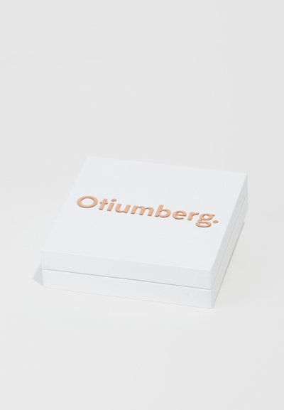 Hvid rektangulær boks med en glat tekstur, der har prægede "Otiumberg." i rosaguld på låget. Enkel og minimalistsk design.
