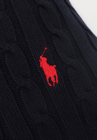 Μαύρο ύφασμα πλεκτό με καλώδιο, με κόκκινο κεντημένο λογότυπο ενός παίκτη πόλο πάνω σε άλογο που κρατά ανυψωμένο ρόπαλο.