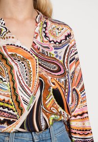Blusa multicolore con motivi a spirale in arancione, rosa e marrone. Materiale leggero con scollatura a V e maniche lunghe.
