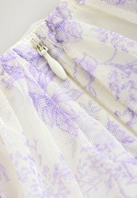 Top in pizzo con motivo floreale lavanda, caratterizzato da una cerniera bianca e una texture a rete. Il tessuto appare leggero e delicato.