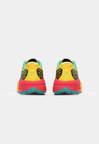 Zapatillas de correr coloridas con parte superior amarilla, acentos negros, detalles turquesas y una entresuela roja. Patrones texturizados distintivos en los laterales.