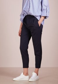 Marineblaue, taillierte Cropped-Hosen mit Taschen an den Seiten und umgeschlagenen Säumen, kombiniert mit weißen Sneakern und einem blau gestreiften Hemd.