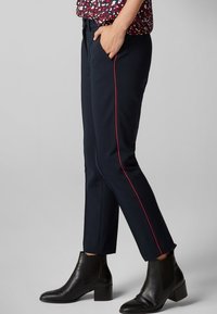 Pantalons navy à coupe slim avec une bande latérale rouge, dotés d'une taille discrète et de poches latérales, associés à des bottines noires à la cheville.