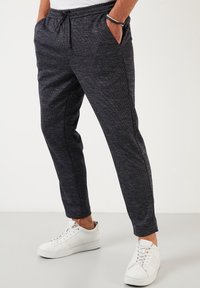 Dark grey athletic joggers with a textured fabric, featuring an elastic waistband with a drawstring and side pockets. Paired with white sneakers.