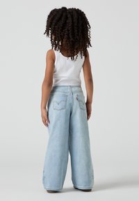 Světlé modré široké džíny z denimu s vysokým pasem, zadními kapsami a květinovou výšivkou na lemu. Nosit s bílým tílkem.