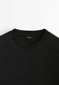 Černé tričko s crew neck výstřihem vyrobené z měkké bavlny, s žebrovaným límcem a jednoduchým, bezešvým designem, bez viditelných vzorů nebo výzdoby.