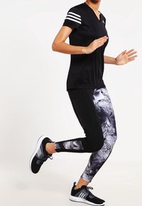 Zwart sport t-shirt met witte gestreepte schouders, gecombineerd met slim-fit leggings met een zwart en grijs abstract patroon. Zwarte hardloopschoenen.