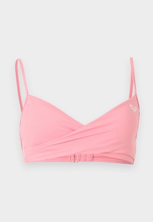 Zachtroze bikinitop met dunne verstelbare bandjes, crossover frontdesign en een klein wit logo op de linkercup tegen een lichte achtergrond.