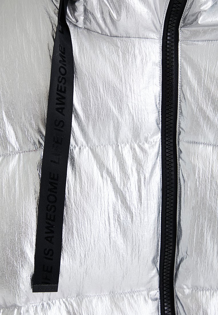 Srebrna kurtka puchowa z błyszczącą, teksturowaną zewnętrzną częścią, czarnym zamkiem błyskawicznym oraz czarną tkana metką z napisem "ŻYCIE JEST WSPANIAŁE."